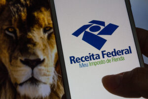 São Paulo, Brazil. February 26, 2021. Internal Revenue Service (IRS) app (Brazilian Receita Federal) - Hand holding a white cell phone with lion image on the background. Selective focus.